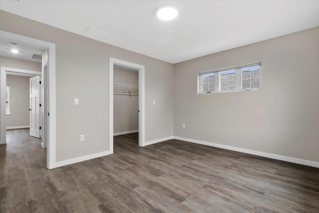 unfurnished bedroom featuring a walk in closet, dark hardwood / wood-style floors, and a closet