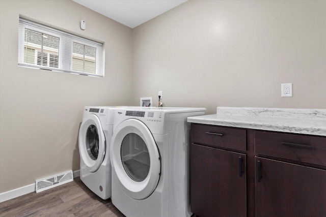 clothes washing area with dark hardwood / wood-style floors, washer and dryer, and cabinets