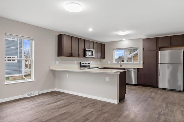 kitchen featuring hardwood / wood-style flooring, dark brown cabinetry, kitchen peninsula, and appliances with stainless steel finishes