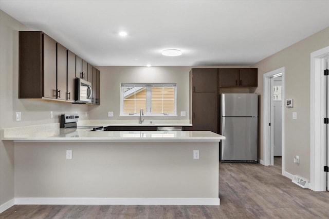 kitchen with kitchen peninsula, dark brown cabinets, stainless steel appliances, and light hardwood / wood-style flooring