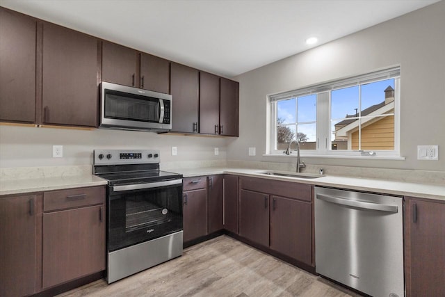 kitchen with dark brown cabinets, stainless steel appliances, light hardwood / wood-style flooring, and sink