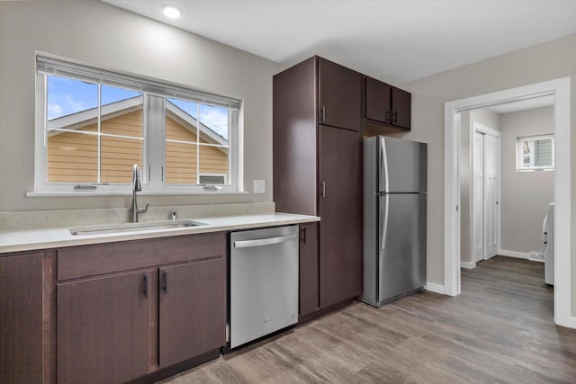 kitchen featuring appliances with stainless steel finishes, light wood-type flooring, dark brown cabinetry, and sink