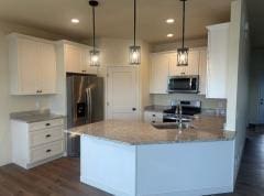 kitchen featuring light stone counters, hanging light fixtures, white cabinetry, stainless steel appliances, and dark hardwood / wood-style flooring