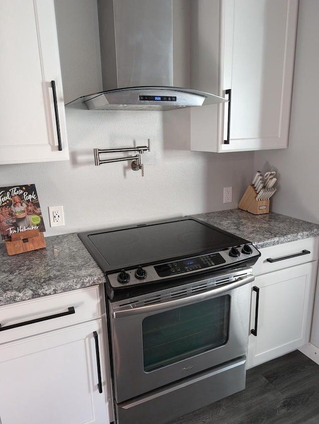 kitchen featuring wall chimney exhaust hood, stainless steel electric range oven, dark hardwood / wood-style flooring, and white cabinets