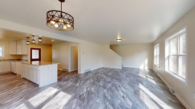 kitchen with white cabinets, pendant lighting, light wood-type flooring, and light stone countertops