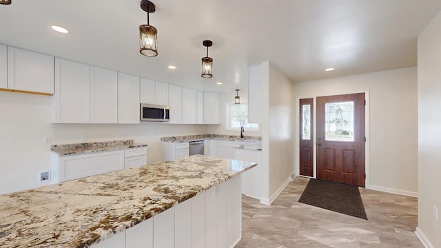 kitchen with appliances with stainless steel finishes, white cabinetry, pendant lighting, and light stone counters