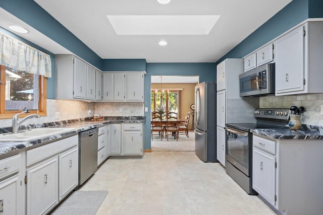 kitchen with decorative backsplash, stainless steel appliances, sink, a skylight, and light tile patterned floors