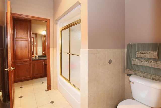 full bathroom featuring toilet, bath / shower combo with glass door, vanity, and tile walls