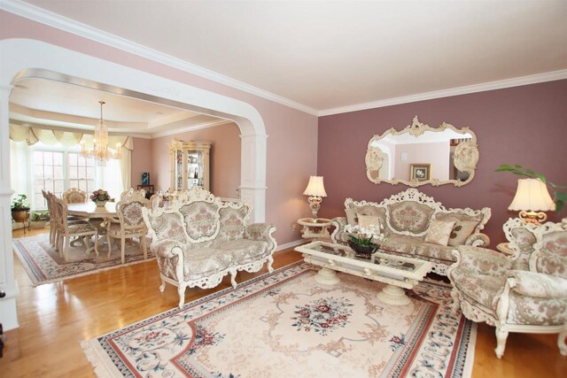 living room with hardwood / wood-style flooring, crown molding, decorative columns, a notable chandelier, and a raised ceiling