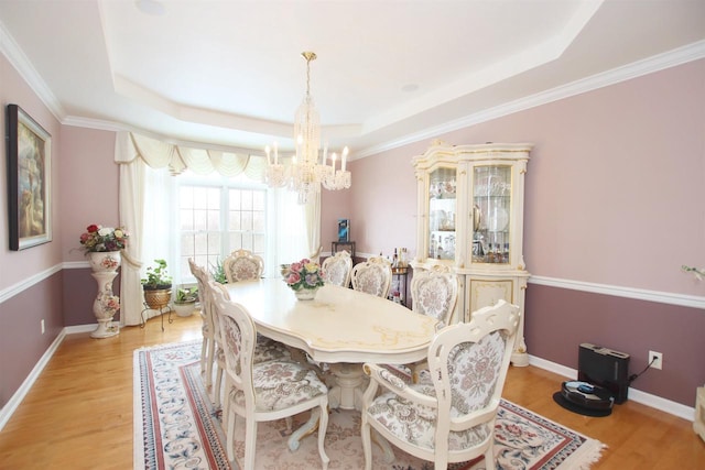 dining area with an inviting chandelier, light wood-type flooring, and a raised ceiling