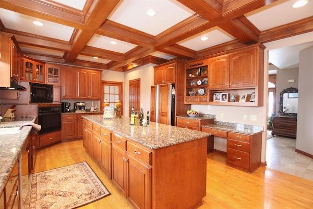 kitchen featuring a kitchen island, light stone countertops, light wood-type flooring, beamed ceiling, and black appliances