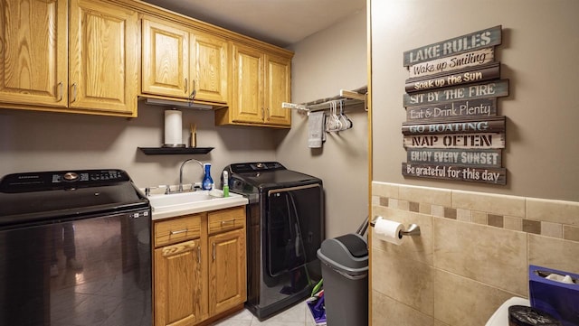 laundry room featuring tile walls, sink, cabinets, washing machine and dryer, and light tile patterned floors