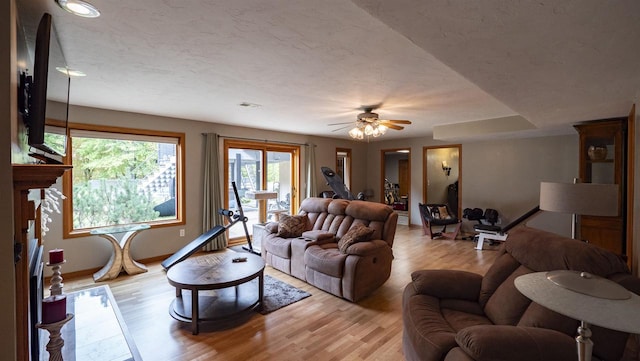 living room with ceiling fan, light hardwood / wood-style floors, and a textured ceiling