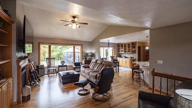 living room with ceiling fan with notable chandelier, light hardwood / wood-style floors, and vaulted ceiling