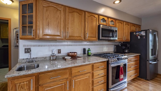 kitchen with light wood-type flooring, light stone countertops, sink, and stainless steel appliances