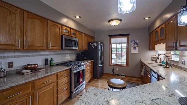 kitchen with light stone counters, pendant lighting, sink, light hardwood / wood-style flooring, and appliances with stainless steel finishes