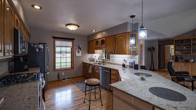 kitchen featuring sink, pendant lighting, light hardwood / wood-style flooring, appliances with stainless steel finishes, and a kitchen bar