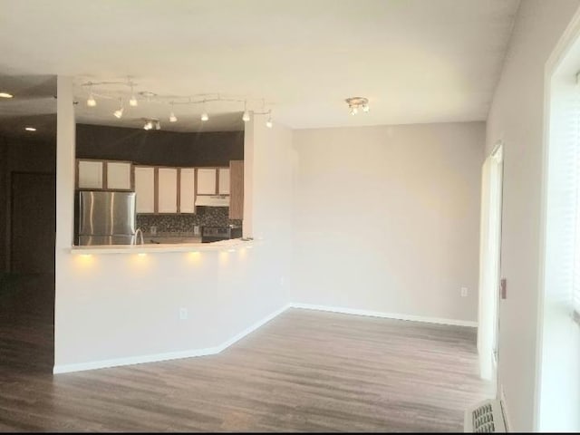 kitchen with track lighting, hardwood / wood-style flooring, stainless steel refrigerator, and backsplash