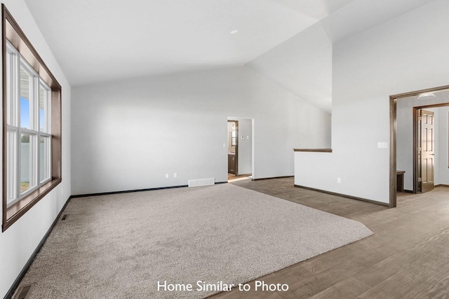 unfurnished living room with high vaulted ceiling and light carpet