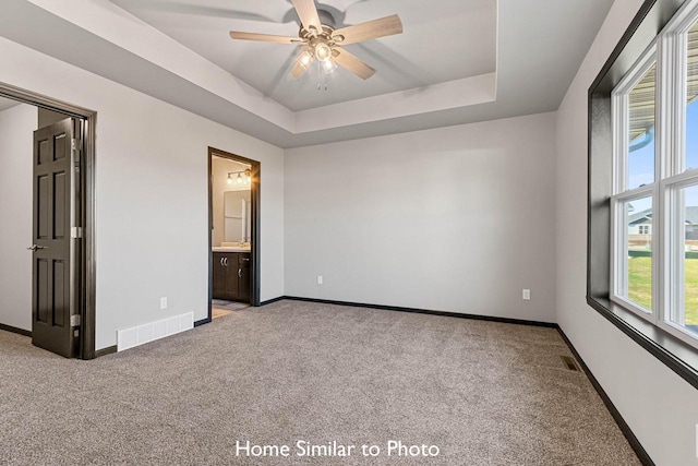 unfurnished bedroom featuring ceiling fan, connected bathroom, a raised ceiling, and light colored carpet