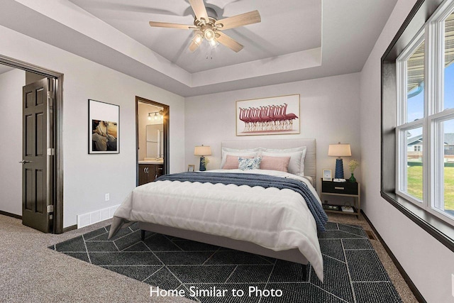 bedroom with dark colored carpet, ceiling fan, connected bathroom, and a raised ceiling