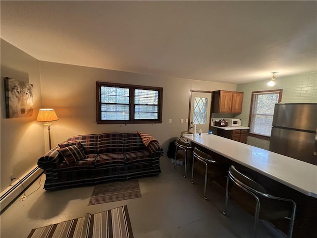 kitchen featuring baseboard heating, stainless steel refrigerator, concrete flooring, and a healthy amount of sunlight