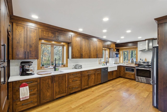 kitchen with tasteful backsplash, light wood-type flooring, sink, wall chimney exhaust hood, and stainless steel appliances