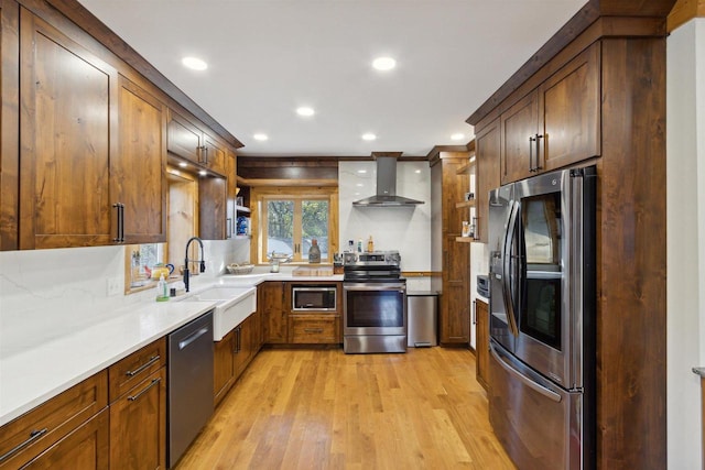 kitchen with appliances with stainless steel finishes, sink, light hardwood / wood-style floors, wall chimney exhaust hood, and light stone counters