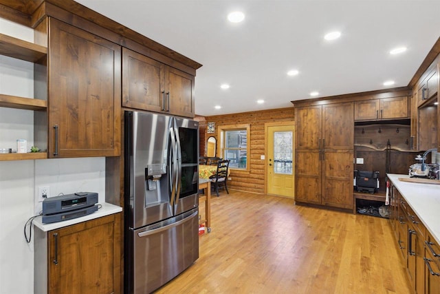 kitchen featuring sink, stainless steel refrigerator with ice dispenser, light wood-type flooring, and wood walls