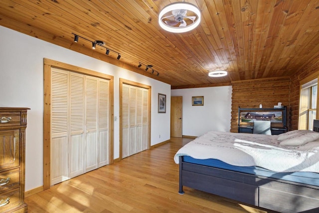 bedroom featuring wooden ceiling, track lighting, light wood-type flooring, and two closets