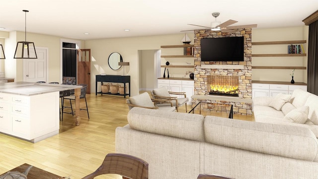 living room featuring a stone fireplace, light wood-type flooring, and ceiling fan