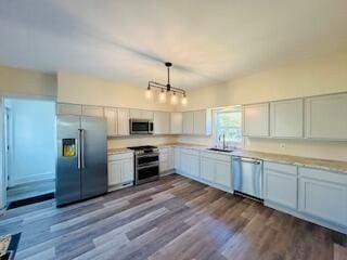 kitchen with white cabinets, hanging light fixtures, sink, stainless steel appliances, and light wood-type flooring