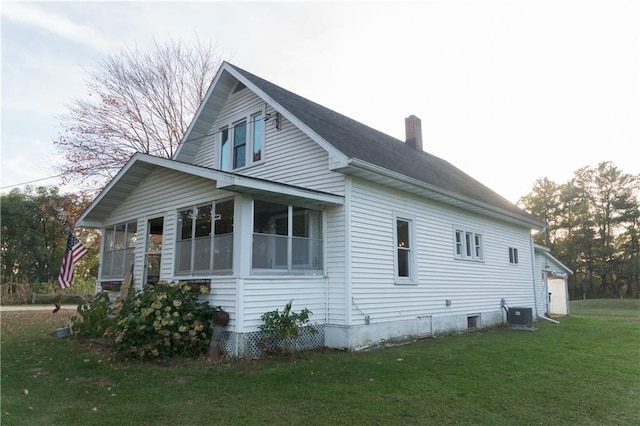 view of property exterior featuring central air condition unit, a sunroom, and a lawn