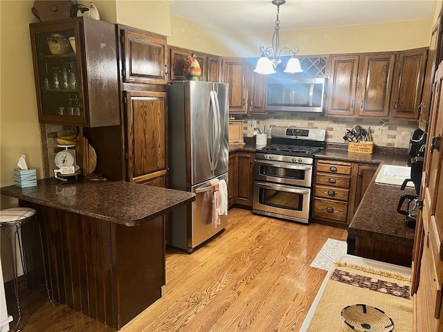 kitchen with hanging light fixtures, backsplash, appliances with stainless steel finishes, a kitchen breakfast bar, and light hardwood / wood-style floors