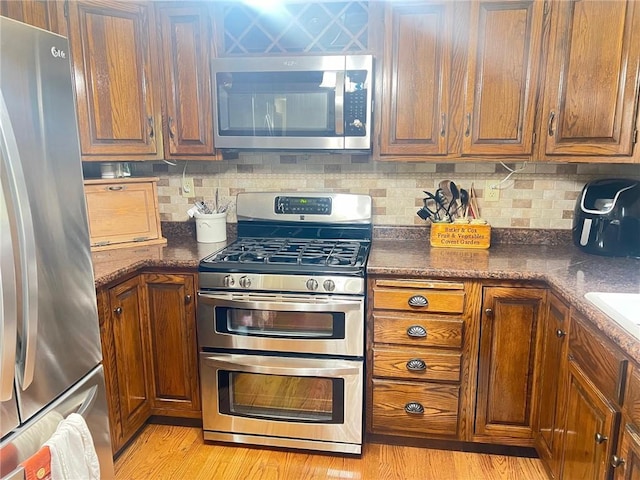 kitchen featuring decorative backsplash, dark stone counters, light hardwood / wood-style floors, and appliances with stainless steel finishes