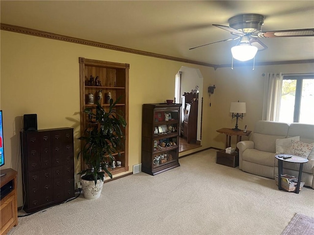 carpeted living room with ornamental molding and ceiling fan