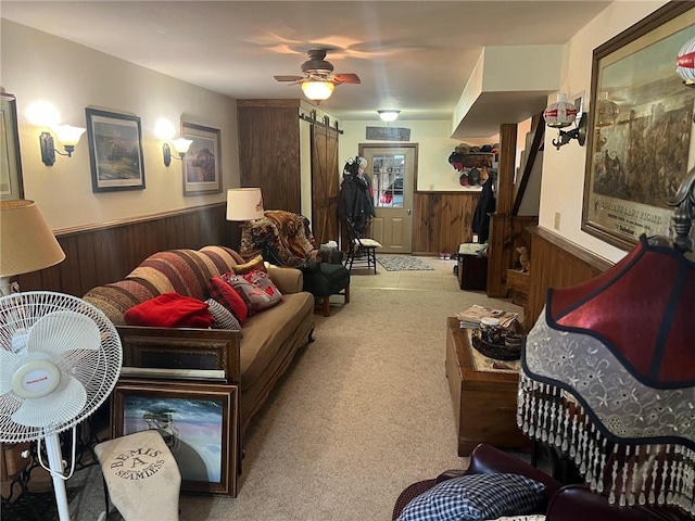 living room with ceiling fan, wood walls, a barn door, and light carpet