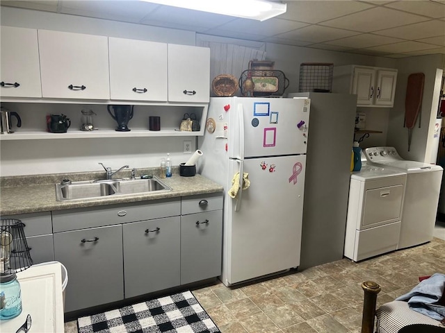 kitchen with white refrigerator, washer and clothes dryer, a paneled ceiling, sink, and white cabinetry