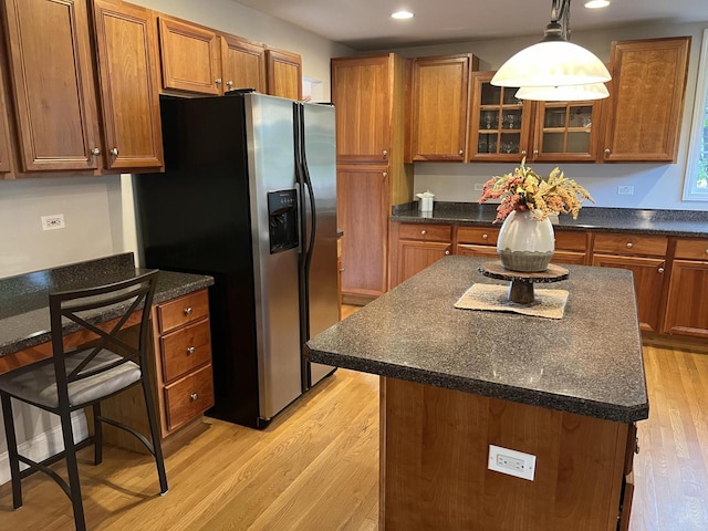 kitchen featuring light wood-type flooring, a kitchen island, a breakfast bar, decorative light fixtures, and stainless steel refrigerator with ice dispenser