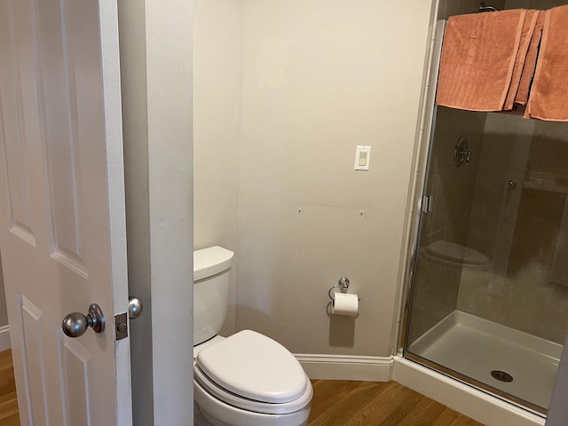 bathroom with hardwood / wood-style flooring, a shower with shower door, and toilet