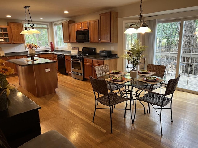 kitchen featuring light wood-type flooring, decorative light fixtures, black appliances, and a center island