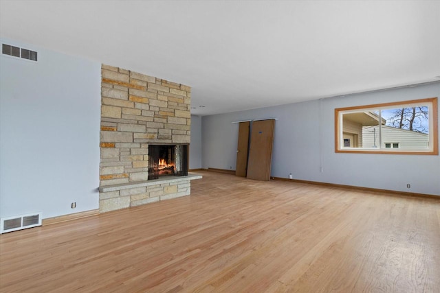 unfurnished living room featuring a stone fireplace and light hardwood / wood-style floors