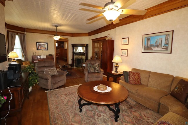 living room featuring ceiling fan, dark hardwood / wood-style flooring, crown molding, and a stone fireplace