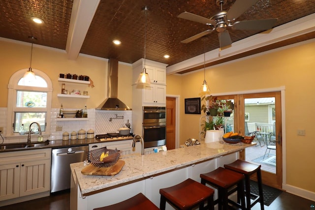 kitchen featuring decorative light fixtures, wall chimney range hood, stainless steel appliances, dark stone counters, and sink