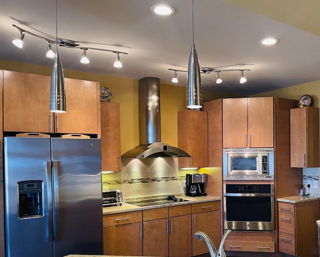 kitchen featuring light stone counters, wall chimney range hood, appliances with stainless steel finishes, decorative light fixtures, and backsplash