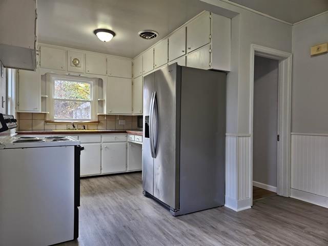 kitchen with stove, backsplash, white cabinetry, stainless steel refrigerator with ice dispenser, and light wood-type flooring