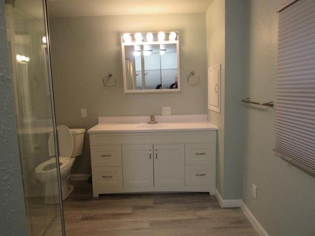 bathroom featuring hardwood / wood-style floors, a shower with shower door, vanity, and toilet