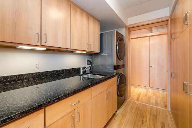 laundry area with light hardwood / wood-style floors, stacked washer / drying machine, sink, and cabinets