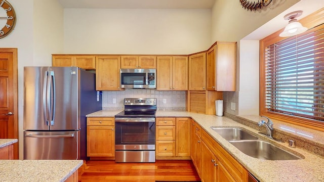 kitchen featuring sink, backsplash, hardwood / wood-style flooring, light stone counters, and stainless steel appliances