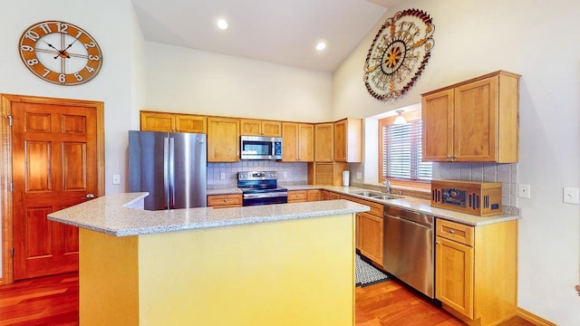 kitchen with sink, high vaulted ceiling, light hardwood / wood-style flooring, appliances with stainless steel finishes, and a kitchen island